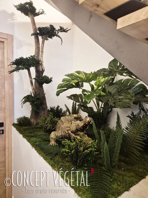 Transformez votre intérieur en un véritable havre de nature avec cet aménagement décoratif d’exception. Niché sous un escalier moderne en bois, ce jardin intérieur met en valeur une composition harmonieuse de plantes luxuriantes, de fougères et de feuilla